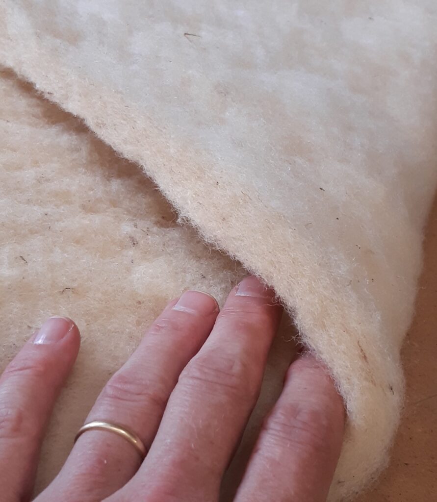 Un morceau de laine douce et naturelle, soulevé pour montrer sa texture. Artisanat local normand.