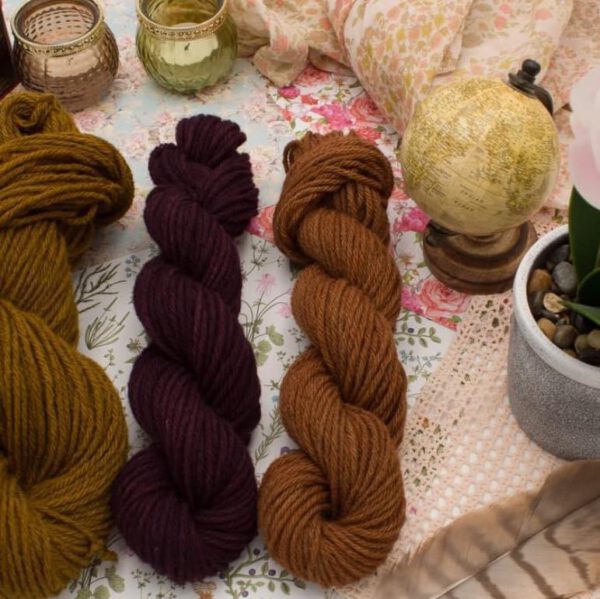 Trois écheveaux de laine de couleurs jaune, violet et marron, présentés sur une table décorative.