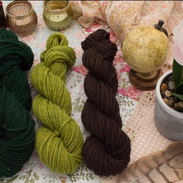 Pelotes de laine de couleurs variées (vert, jaune, marron) sur un fond floral, illustrant la durabilité de l'entreprise.