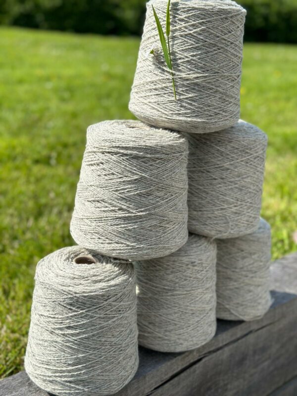 Cônes de laine de mouton empilés sur un fond de gazon, illustration de la production durable de l'entreprise Laines sous les Pommiers.