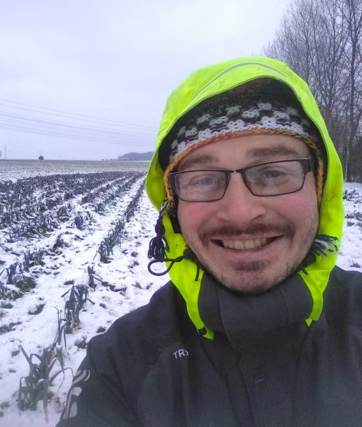 Homme souriant en veste jaune, posé dans un champ enneigé, représentant l'engagement de Laines sous les Pommiers envers la durabilité.