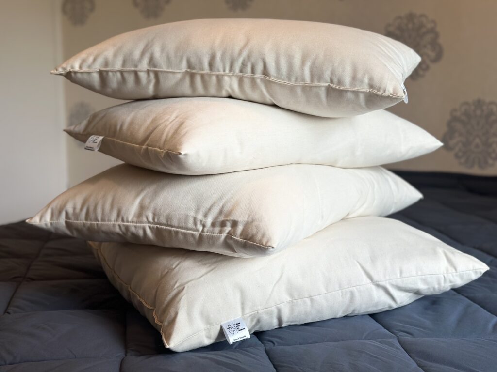 Quatre coussins en laine de mouton, empilés sur un lit, mettant en valeur un design durable et respectueux de l'environnement.