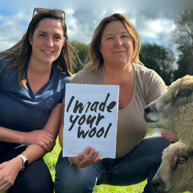 Deux femmes tenant une pancarte "I made your wool" avec des moutons sur un champ, représentant l'entreprise Laines sous les Pommiers.