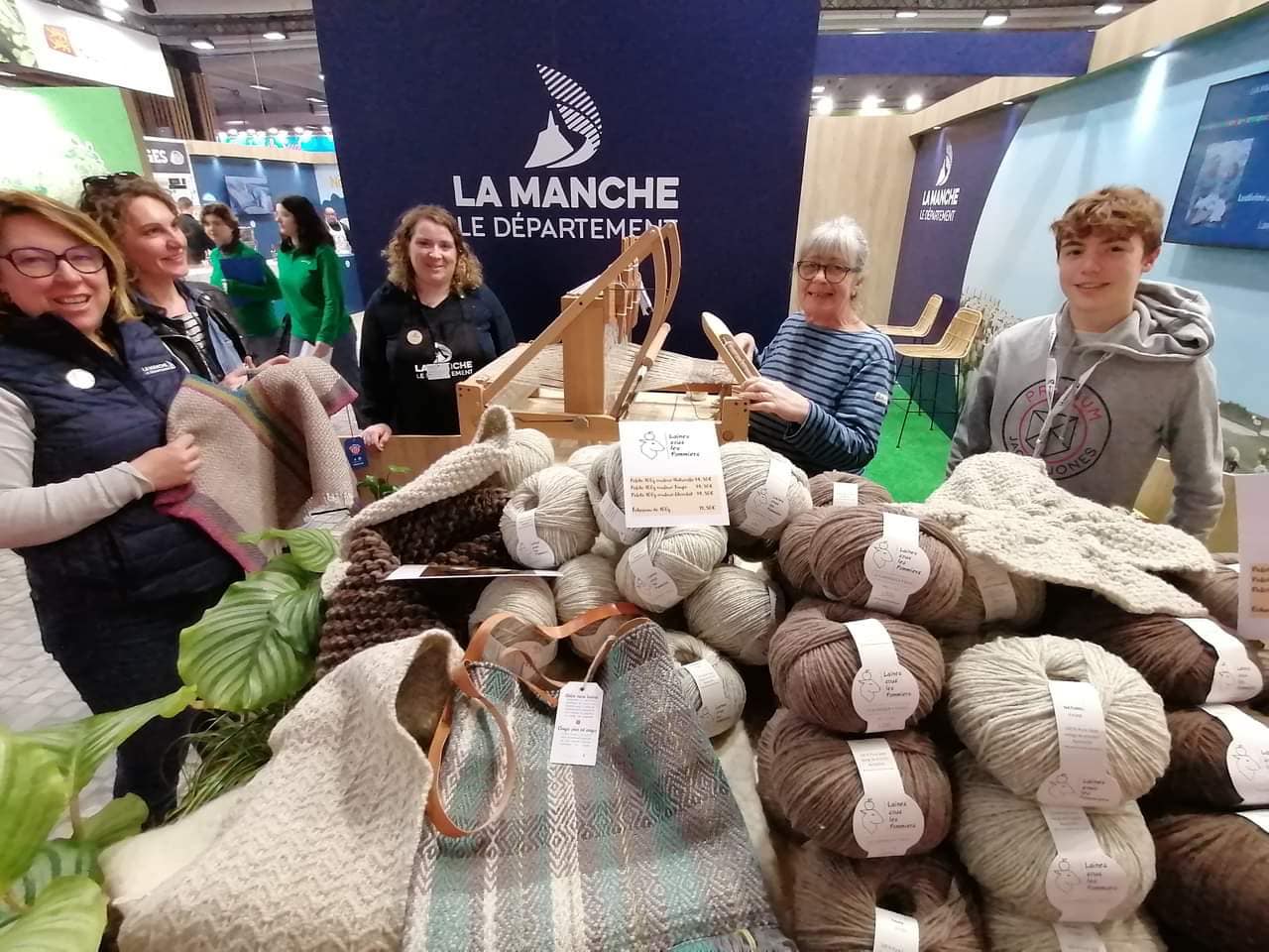 Stand de Laines sous les Pommiers présentant des pelotes de laine et des créations textiles durables, avec des visiteurs engagés.