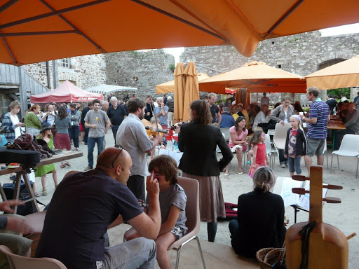 Rassemblement festif sous des parasols, avec des musiciens et des visiteurs engagés dans des activités communautaires.