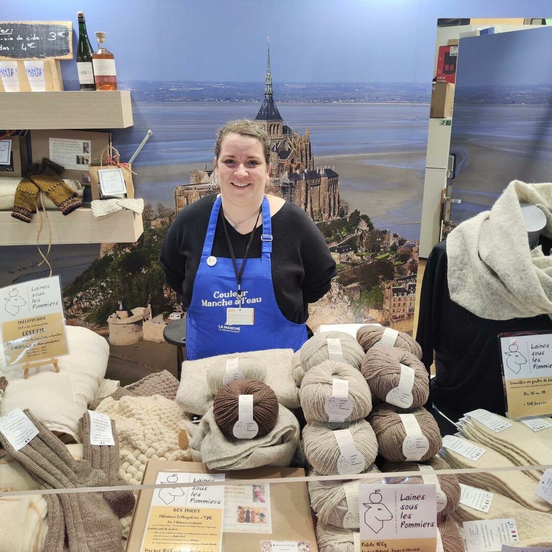 Femme souriante devant un stand de Laines sous les Pommiers, présentant des produits en laine durables et respectueux de l'environnement.