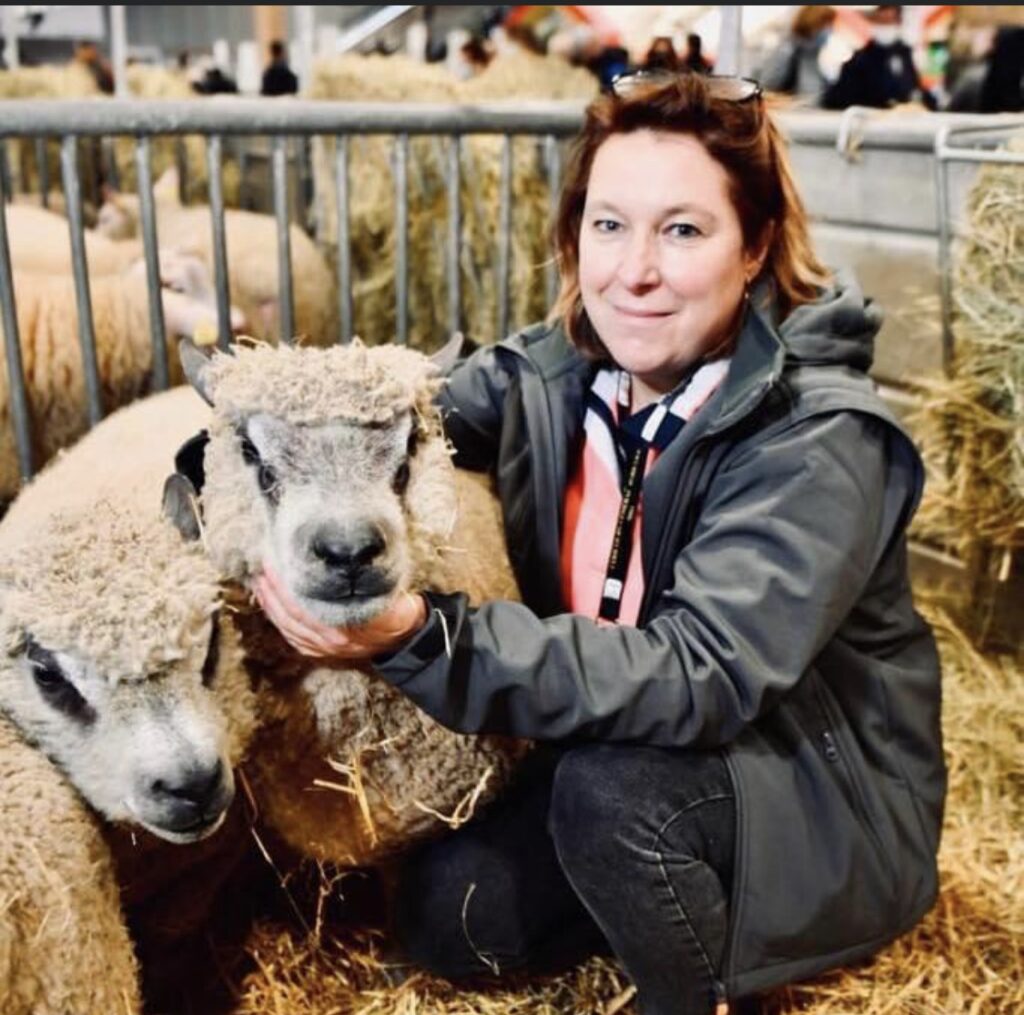 Femme posant avec deux moutons dans une étable, mettant en valeur la production de laine durable.