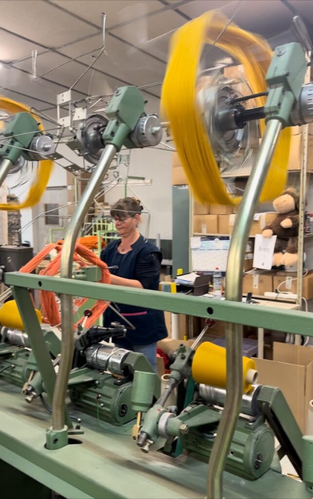 Femme travaillant sur une machine de transformation de laine, entourée de pelotes colorées dans un environnement respectueux de l'environnement.