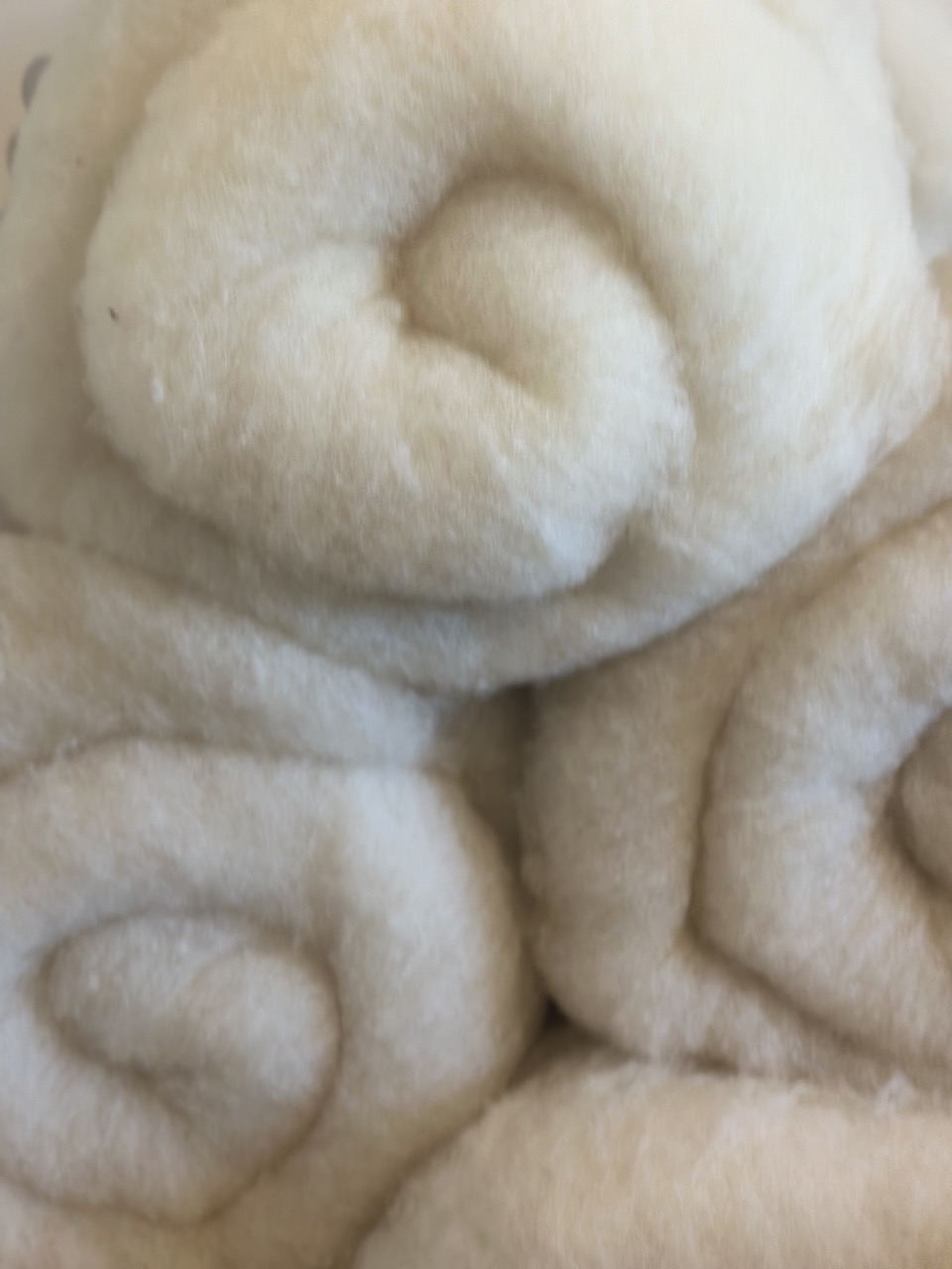 Laine cardée blanche enroulée, utilisée pour des produits artisanaux comme écharpes et coussins, valorisant la production locale normande.