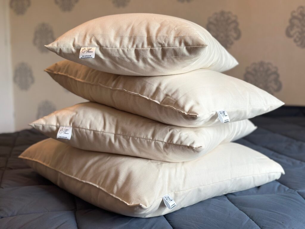 Trois coussins en textile naturel, étiquetés, empilés sur un lit aux draps bleu foncé.