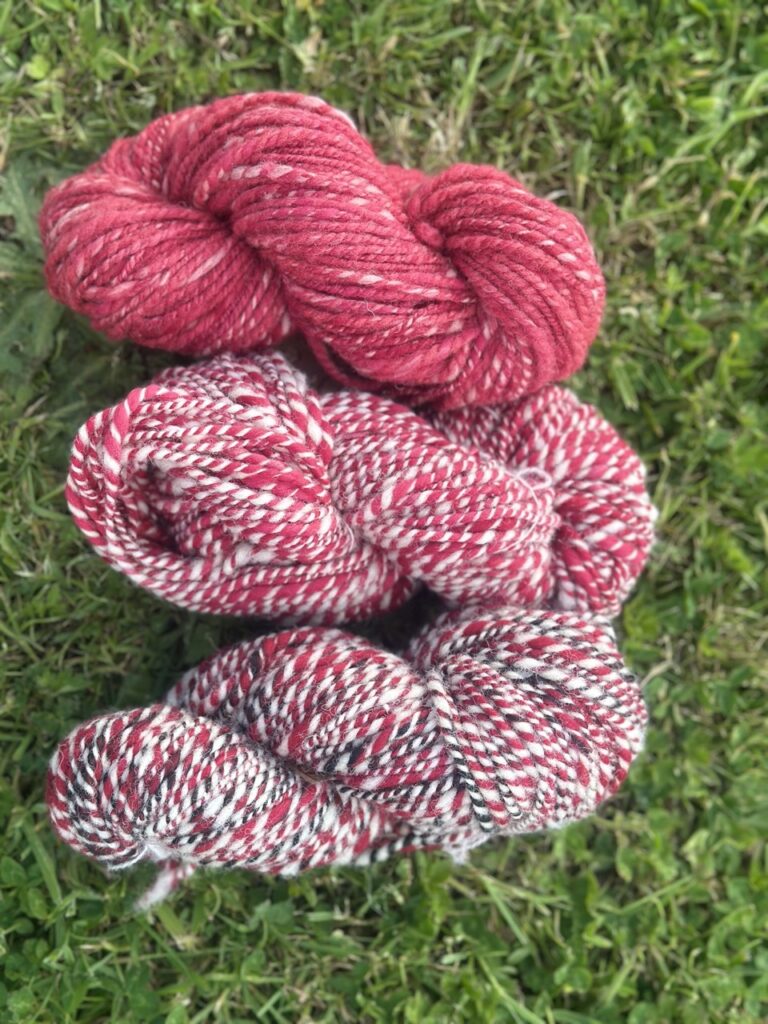 Écheveaux de laine filée main en rouge et motifs, signés Rouge Garance, sur un fond de gazon.
