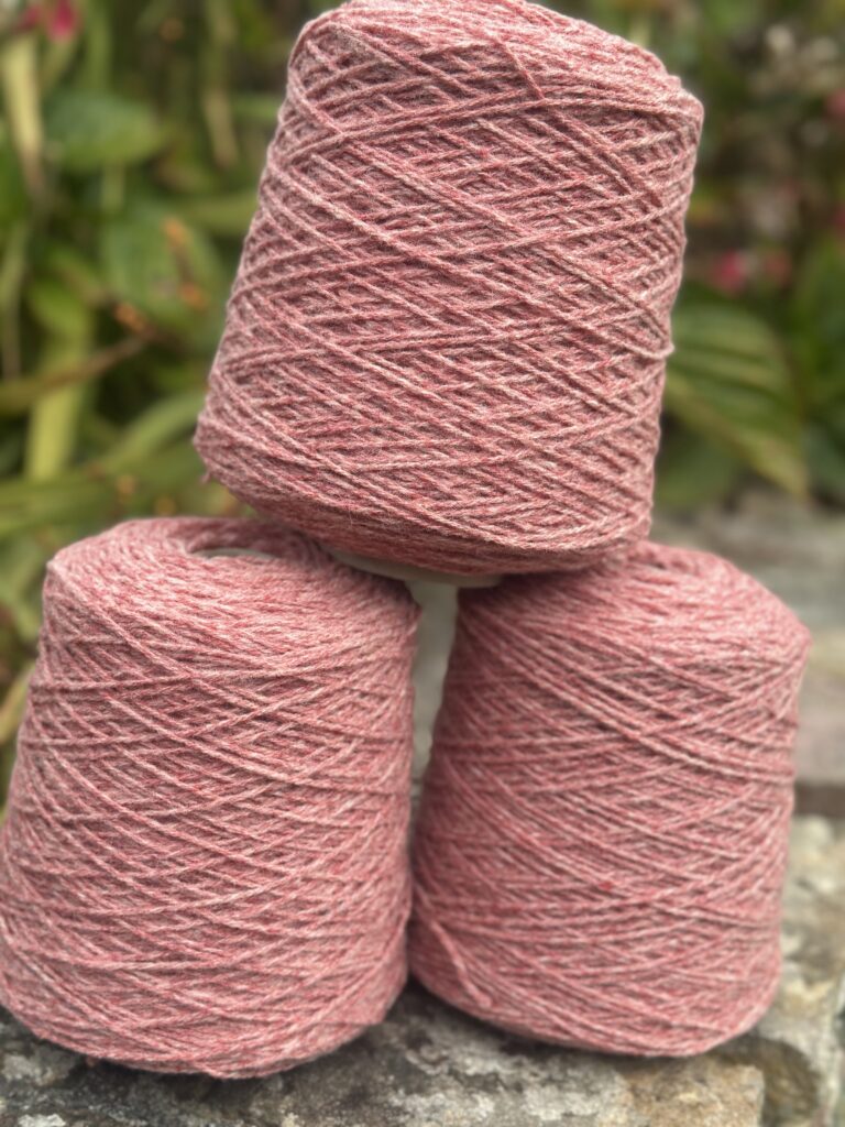 Trois pelotes de laine rose empilées sur une pierre, avec un arrière-plan flou de verdure.