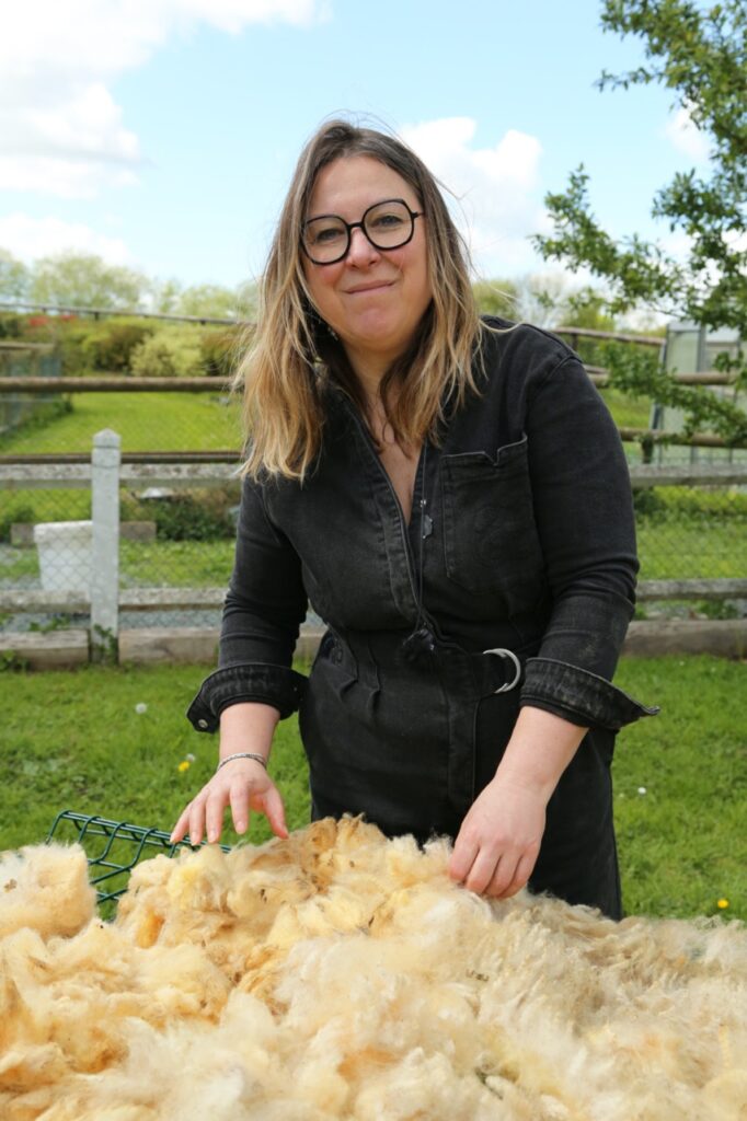 Femme en tenue noire manipulant de la laine sur une table en plein air, entourée de verdure et de pommiers normands.